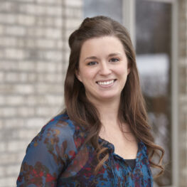 Female dental team member smiling in front of the dental office building